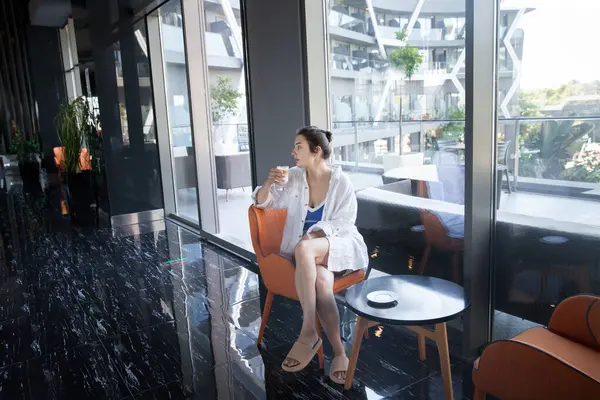 Kız lobide kahve içiyor ve başka tarafa bakıyor.