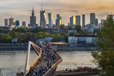 Warszawa, Polonya - 9 Nisan 2024: Varşova şehir merkezinin panoramik manzarası, yeni açılan yaya ve bisiklet köprüsünün modern şekli tarafından çerçevelenmiş, canlı bir anıt ve modern gökdelenler karışımına sahip..