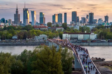 Warszawa, Polonya - 9 Nisan 2024: Varşova şehir merkezinin panoramik manzarası, yeni açılan yaya ve bisiklet köprüsünün modern şekli tarafından çerçevelenmiş, canlı bir anıt ve modern gökdelenler karışımına sahip..