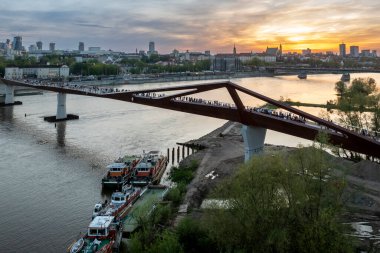 Warszawa, Polonya - 9 Nisan 2024: Varşova şehir merkezinin panoramik manzarası, yeni açılan yaya ve bisiklet köprüsünün modern şekli tarafından çerçevelenmiş, canlı bir anıt ve modern gökdelenler karışımına sahip..
