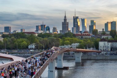 Warszawa, Polonya - 9 Nisan 2024: Varşova şehir merkezinin panoramik manzarası, yeni açılan yaya ve bisiklet köprüsünün modern şekli tarafından çerçevelenmiş, canlı bir anıt ve modern gökdelenler karışımına sahip..