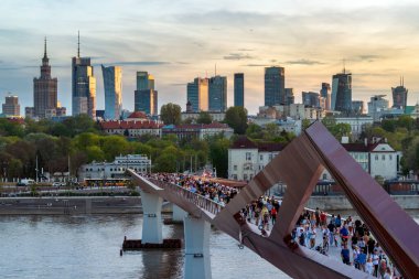 Warszawa, Polonya - 9 Nisan 2024: Varşova şehir merkezinin panoramik manzarası, yeni açılan yaya ve bisiklet köprüsünün modern şekli tarafından çerçevelenmiş, canlı bir anıt ve modern gökdelenler karışımına sahip..