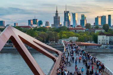 Warszawa, Polonya - 9 Nisan 2024: Varşova şehir merkezinin panoramik manzarası, yeni açılan yaya ve bisiklet köprüsünün modern şekli tarafından çerçevelenmiş, canlı bir anıt ve modern gökdelenler karışımına sahip..
