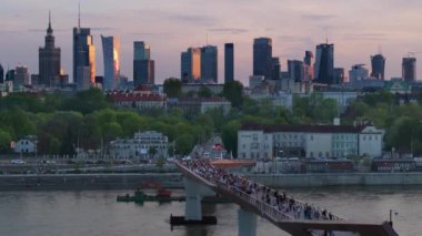 Warszawa, Polonya - 9 Nisan 2024: Varşova şehir merkezinin panoramik manzarası, yeni açılan yaya ve bisiklet köprüsünün modern şekli tarafından çerçevelenmiş, canlı bir anıt ve modern gökdelenler karışımına sahip..
