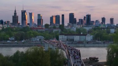 Warszawa, Polonya - 9 Nisan 2024: Varşova şehir merkezinin panoramik manzarası, yeni açılan yaya ve bisiklet köprüsünün modern şekli tarafından çerçevelenmiş, canlı bir anıt ve modern gökdelenler karışımına sahip..