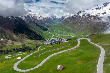 The alpine village of Andermatt surrounded by green meadows, and snowy peaks in the background, Canton of Uri, Switzerland, Europe clipart