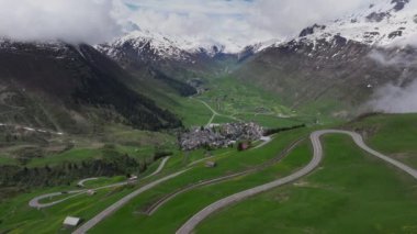 Andermatt 'ın yeşil çayırlarla çevrili dağlık köyü ve arka planda karlı tepeler, Uri Kantonu, İsviçre, Avrupa