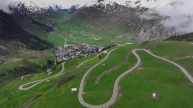 Andermatt 'ın yeşil çayırlarla çevrili dağlık köyü ve arka planda karlı tepeler, Uri Kantonu, İsviçre, Avrupa