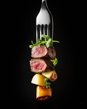 Yemek fotoğrafçılığı: Kesilmiş bir parça sığır eti ve üzerinde küçük bir dilim yeşil yiyecek olan bir çatal, siyah bir arka plana karşı., 