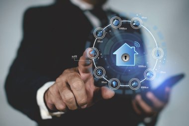 Akıllı telefon konseptinde akıllı ev dijital uzaktan kumanda. Teknoloji kontrolündeki şeylerin interneti. Sanal akıllı ev simgesi işlevi gören bir işadamı eve dokunuyor.