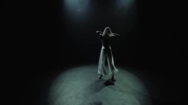 Spot ışıklarıyla modern dans eden bir kadın. Çağdaş dans. Genç dansçı karanlık sahnede oynuyor. 4K 'da yakın plan, UHD