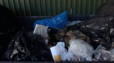 Çeşitli atık ve çöp türleriyle dolu dağınık bir çöp konteynırı, kentsel atık yönetimi sorunları sergileniyor.