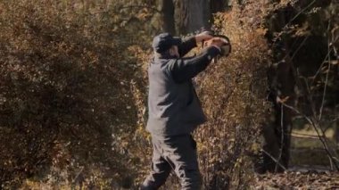 Huzurlu ve huzurlu bir sonbahar ormanında etkili bir şekilde odun kesmek için güçlü bir testereyi ustalıkla kullanan bir adam.