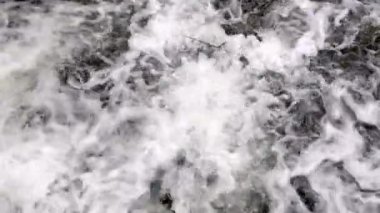 Dağ nehri su yüzeyi ağır çekimde. Dağ nehrinde dalgalar oluşturan temiz bir dere. Akan su arka planına yakın çekim. Taştan akıntılar arasında akan hızlı bir akış. Dağ nehrinin yakınına. Yüksek