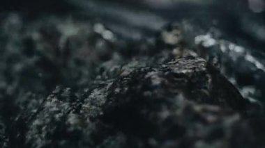 Karanlık taşların üzerinde akan suyun yakın çekim görüntüsü, huzur verici ve huzurlu bir atmosfer yaratır.
