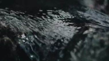 Karanlık taşların üzerinde akan suyun yakın çekim görüntüsü, huzur verici ve huzurlu bir atmosfer yaratır.