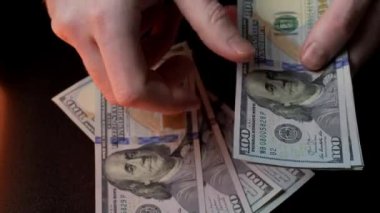 Eller titizlikle koyu bir yüzeye serilmiş sayısız dolarlık banknotları sayıyor.