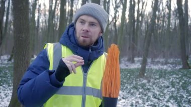 Çelik yelek giyen biri, karlı bir orman manzarasını kazar ve kışın açık hava aktivitelerini sergiler..