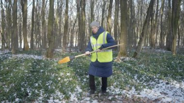 Çelik yelek giyen biri, karlı bir orman manzarasını kazar ve kışın açık hava aktivitelerini sergiler..