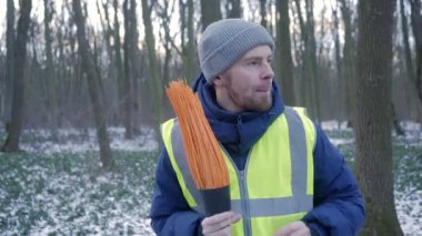 Çalışkan bir işçi parlak bir yelekle giyinmiş, sakin bir ormanda karla kaplı bir patika boyunca yürüyor.