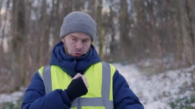 Çelik yelek giyen biri, karlı bir orman manzarasını kazar ve kışın açık hava aktivitelerini sergiler..