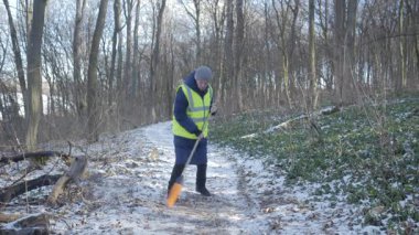 Bir gönüllü, karlı bir patikayı temizliyor. Çevresel koruma ve toplum ruhuna olan bağlılığını gösteriyor..