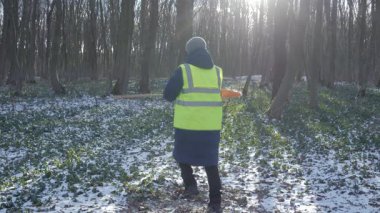 Soğuk için tam teçhizatlı bir insan, elinde bir kürek tutarken güvenli bir şekilde karlı bir ormanda poz verir.