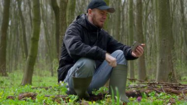 Sakin bir orman ortamında otururken akıllı telefon kullanan bir adam dışarıdaki bağlantıyı vurguluyor..