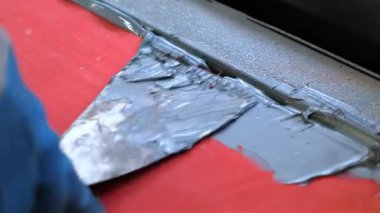 Bu, detaylı onarım çalışmaları sırasında canlı kırmızı bir yüzey üzerinde epoksi uygulamasını gösteren yakın plan bir görüntüdür.