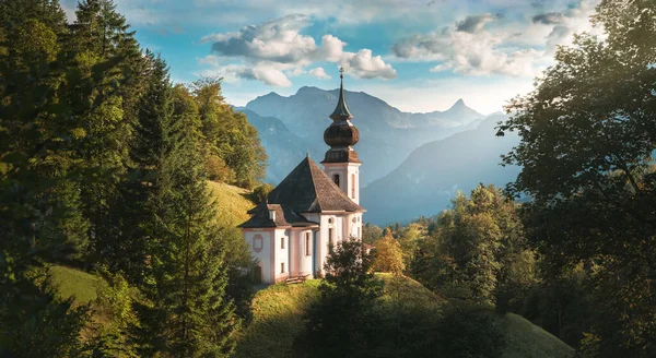 Idyllic little church in the heart of nature, scenic German Alps landscape in Berchtesgaden with mountains in the background, blue sky and lush trees