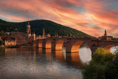 The Old Bridge in Heidelberg, Germany, with dramatic orange light at sunset. Colorful clouds in the sky and naturally illuminated arches of the architecture clipart