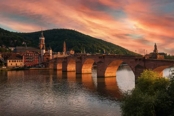 Heidelberg, Almanya 'daki Eski Köprü, gün batımında dramatik turuncu ışık. Gökyüzündeki renkli bulutlar ve mimarinin doğal olarak aydınlatılmış kemerleri.