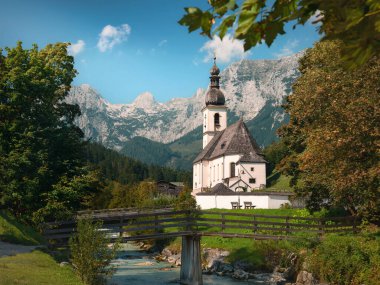 Ramsau 'nun Berchtesgaden, Bavyera, Almanya' daki Alpler 'deki ikonik manzarası. Dağlar, kadın, mavi gökyüzü ve nehir beyaz kiliseyi çevreledi..
