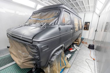 Antika bir minibüsün restorasyonu için hazırlık yapılıyor ve termal sprey boya kabininin içinde gri boya tamamlanıyor. Özenli işçilik ve otomotiv rehabilitasyonundaki detaylara dikkat.