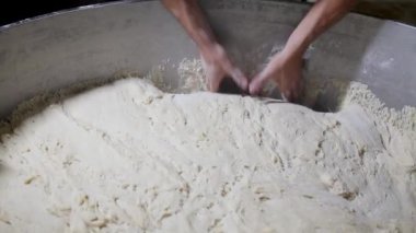 Bir fırıncı hamur karıştırıcıdan hamuru çıkarır ve onu pişirmeden önce şekillendirmek için çalışma masasına yerleştirir. Sahne, geleneksel ekmek yapma sanatını yakalıyor.