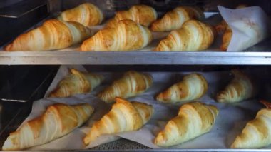 İki tepside kruvasanların elektrikli fırında piştiğini gösteren bir zaman atlaması. Kruvasanlar pişerken altın rengi kahverengiye dönerler. Hamurdan taze pişmiş hamur köftesine lezzetli bir dönüşüm yakalarlar..