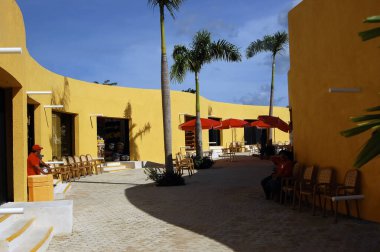Cozumel, Meksika 'da canlı bir açık hava alışveriş merkezi. Parlak sarı duvarlar, sallanan palmiyeler ve hareketli tropikal bir atmosfer. Renkli mimari, yemyeşil sıcak ve davetkar bir ortam yaratır..