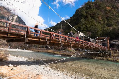 Nagano, JAPAN - 12 Kasım 2024: Kappa Bashi Köprüsü Azusa Nehri 'nin açık suları üzerinde dağlar ve gökyüzü Kamikochi, Nagano Bölgesi, Japonya