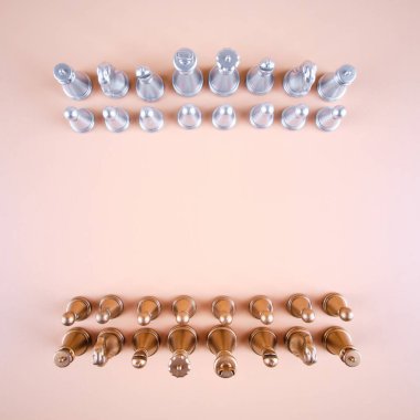 Gold and silver chess pieces on a beige background, top view.