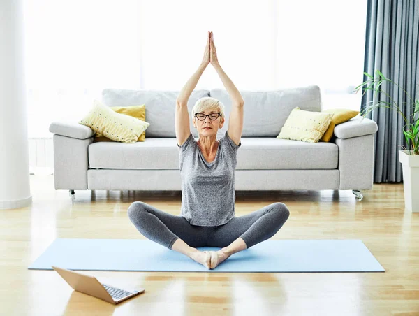 Senior woman exercise stretching yoga using laptop online instructions at home health care