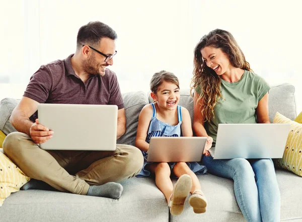 father, mother and daughter having fun doing homework with laptop at home
