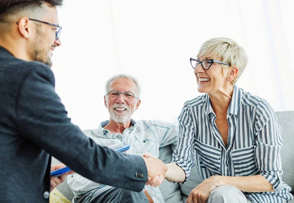 Happy senior old family couple clients make financial insurance estate business deal handshake agent lawyer, satisfied mature customers shake hand meeting bank manager agree on investment contract