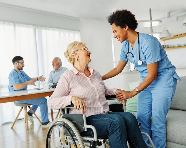 Doctor or nurse caregiver helping senior woman in a wheelchair at home or nursing home