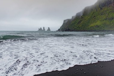 Siyah bir kumsaldan denizdeki kayalık oluşumlar, kıyıya vuran dalgalar..