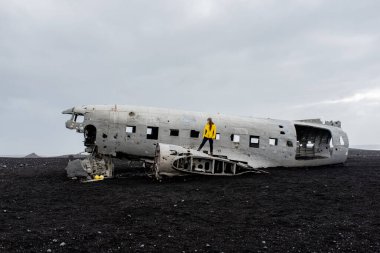 Terk edilmiş bir uçak kazası ve üstünde siyah bir volkanik plajda duran bir adam.