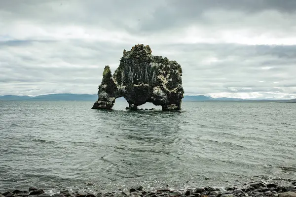 stock image Majestic Sea Stack in Ocean with Mountainous Backdrop and Cloudy Sky