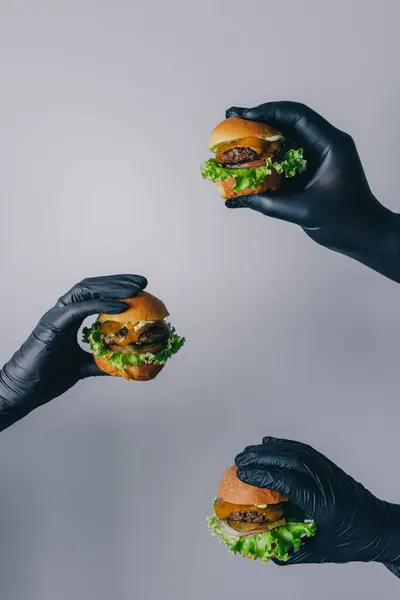 Mini burgerler ellerinde ve gri arkaplanda taze salata var.