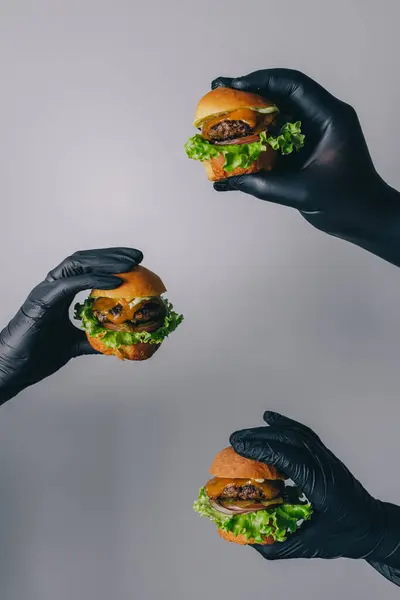 Mini burgerler ellerinde ve gri arkaplanda taze salata var.