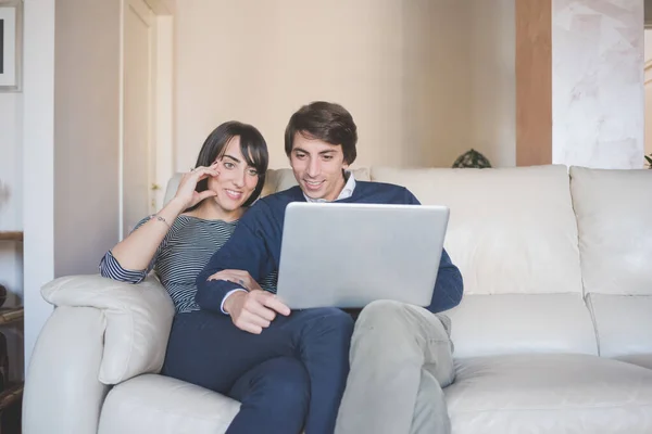 笑顔若いですカップル座ってソファ屋内でホーム使用してコンピュータショッピングオンラインまたはストリーミングビデオ — ストック写真