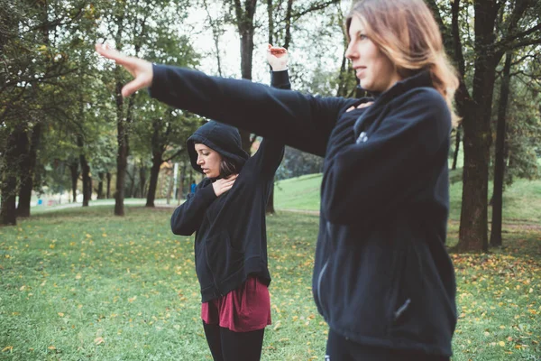 二つのアクティブなスポーツ女性がパーカーを着て屋外公園を伸ばし — ストック写真